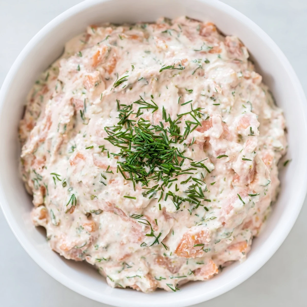 Creamy smoked salmon dip garnished with fresh dill, served with crackers and lemon wedges on a rustic wooden table.