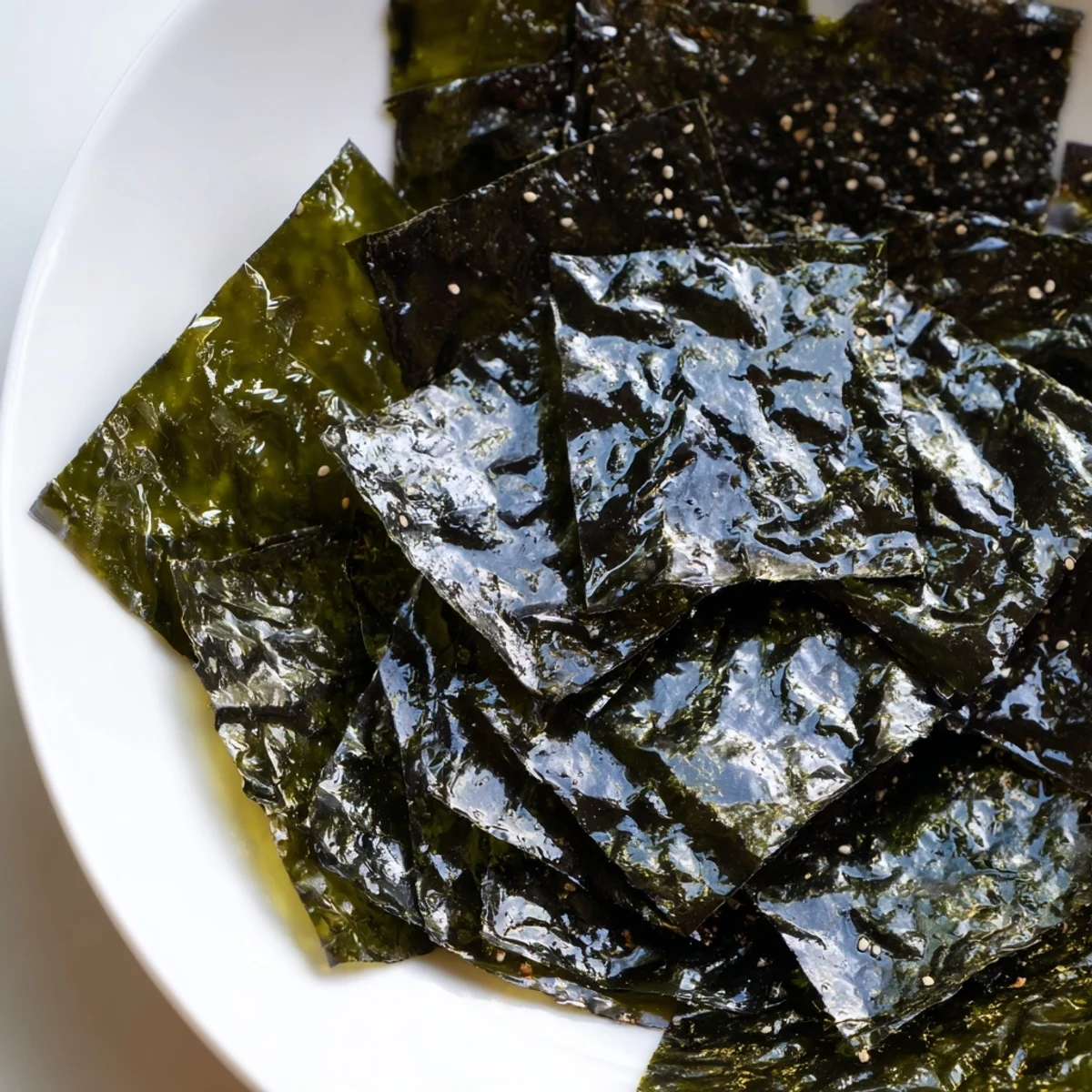 Golden-brown roasted seaweed chips stacked neatly on a bamboo tray, showcasing their light, crispy layers and scattered sesame salt crystals for a simple, savory vegan snack.