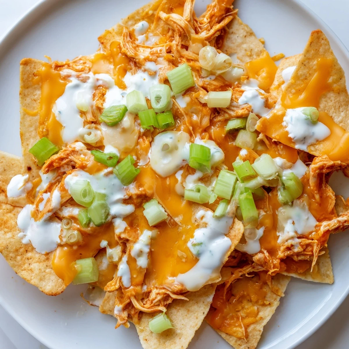 Buffalo Chicken Nachos baked until bubbly, featuring crisp tortilla chips loaded with spicy chicken, melted cheese, and a cool ranch drizzle, garnished with diced tomatoes and cilantro.  