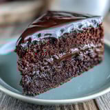 A slice of Easy Chocolate Fudge Cake reveals a squidgy crumb and silky-smooth chocolate icing on a rustic plate.