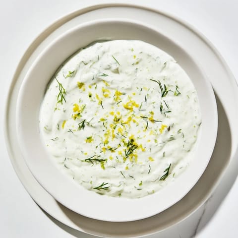 A freshly made Greek Yogurt Herb Dip surrounded by crunchy pita chips and colorful vegetable crudités on a white plate. 