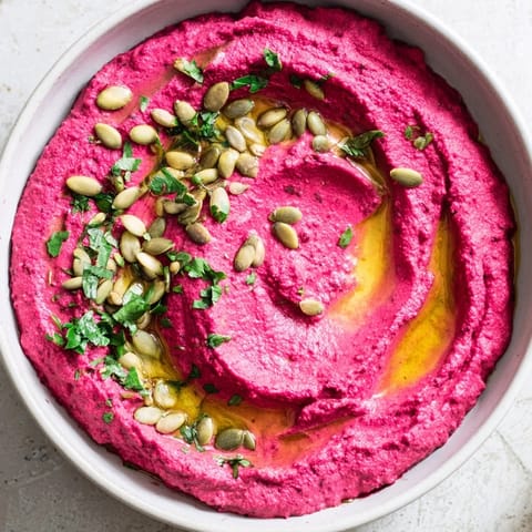 This beet hummus recipe shows a smooth, bright magenta dip garnished with parsley, ready for vegetable crudités.  