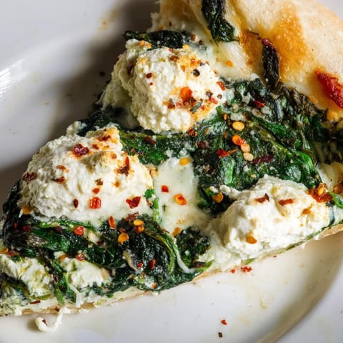 Spinach Ricotta Pizza slices on a white plate, topped with melted mozzarella, fresh parsley, and a hint of red pepper flakes.