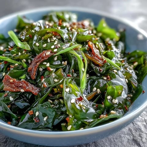A close-up of vibrant Japanese seaweed salad glistening with sesame-ginger dressing and topped with fresh cilantro and sesame seeds.