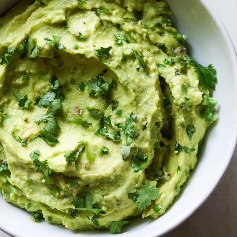 Bright green avocado lime dip garnished with cilantro, garlic, and jalapeño slices in a rustic ceramic bowl.  