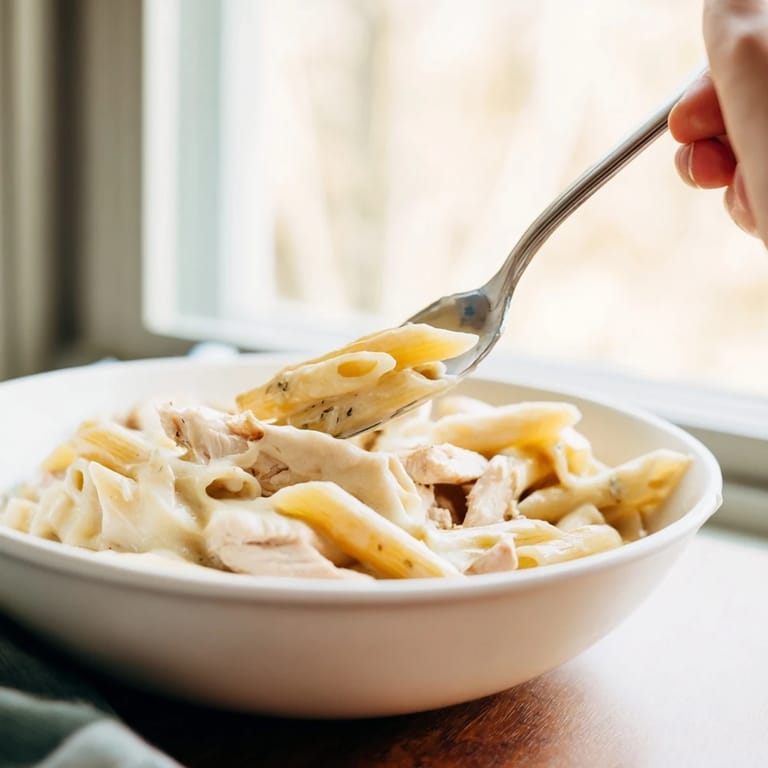Steam rises from a slice of the hearty Chicken Alfredo Casserole, showing gooey cheese pulls and a rich, creamy sauce.